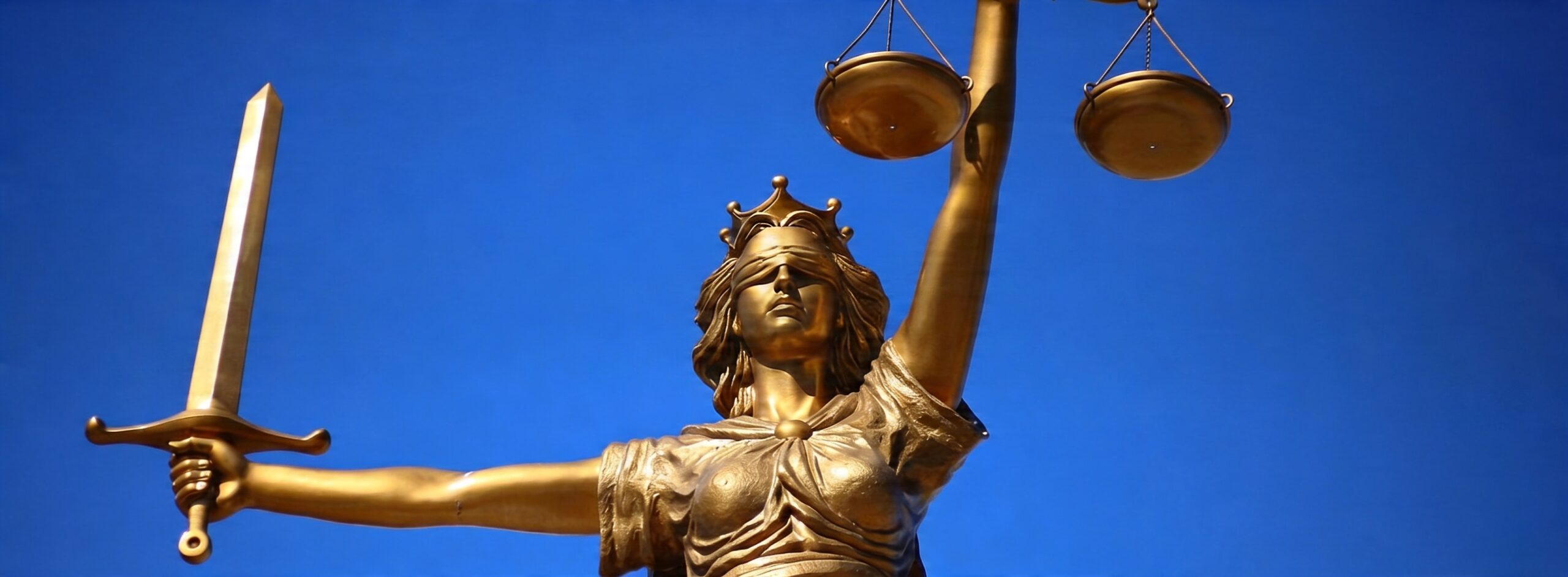 Statue of Lady Justice holding a sword and scales against a blue sky.